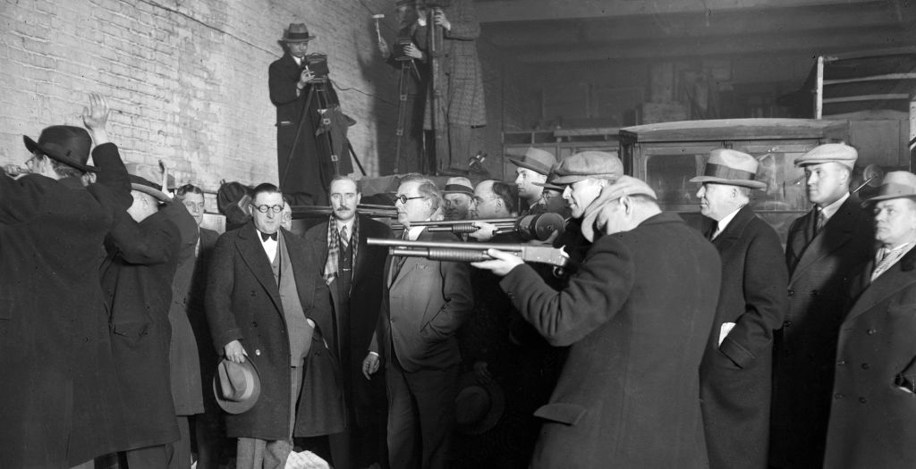 Group of men in suits and hats at an indoor shooting range; some aim rifles while others observe, invoking a historical or investigative context