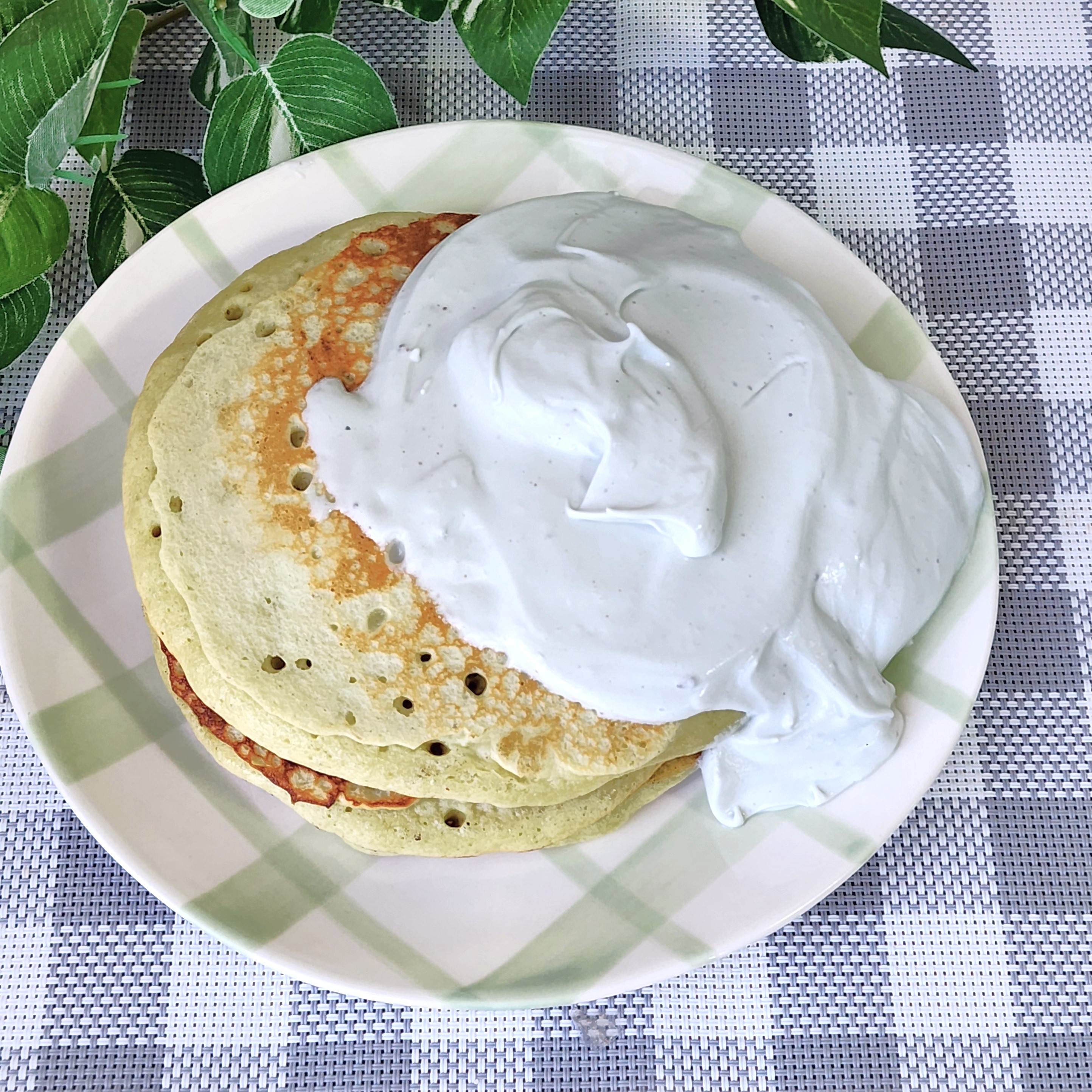 白いソースがかかったパンケーキが皿に載り、テーブルクロスと葉が背景に映える。