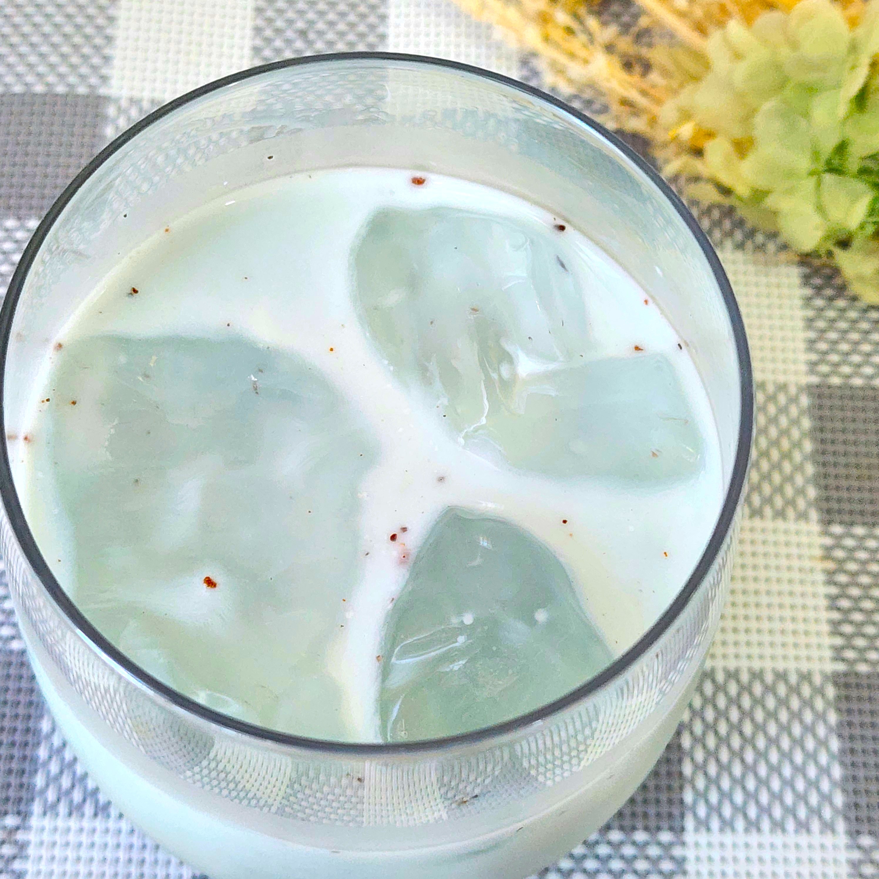 透明な氷が入ったミルクのグラス。背景に花が添えられた飲み物の広告イメージ。