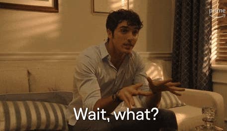 A person sitting on a couch making an expressive gesture, appearing surprised. The phrase "Wait, what?" is overlaid on the image