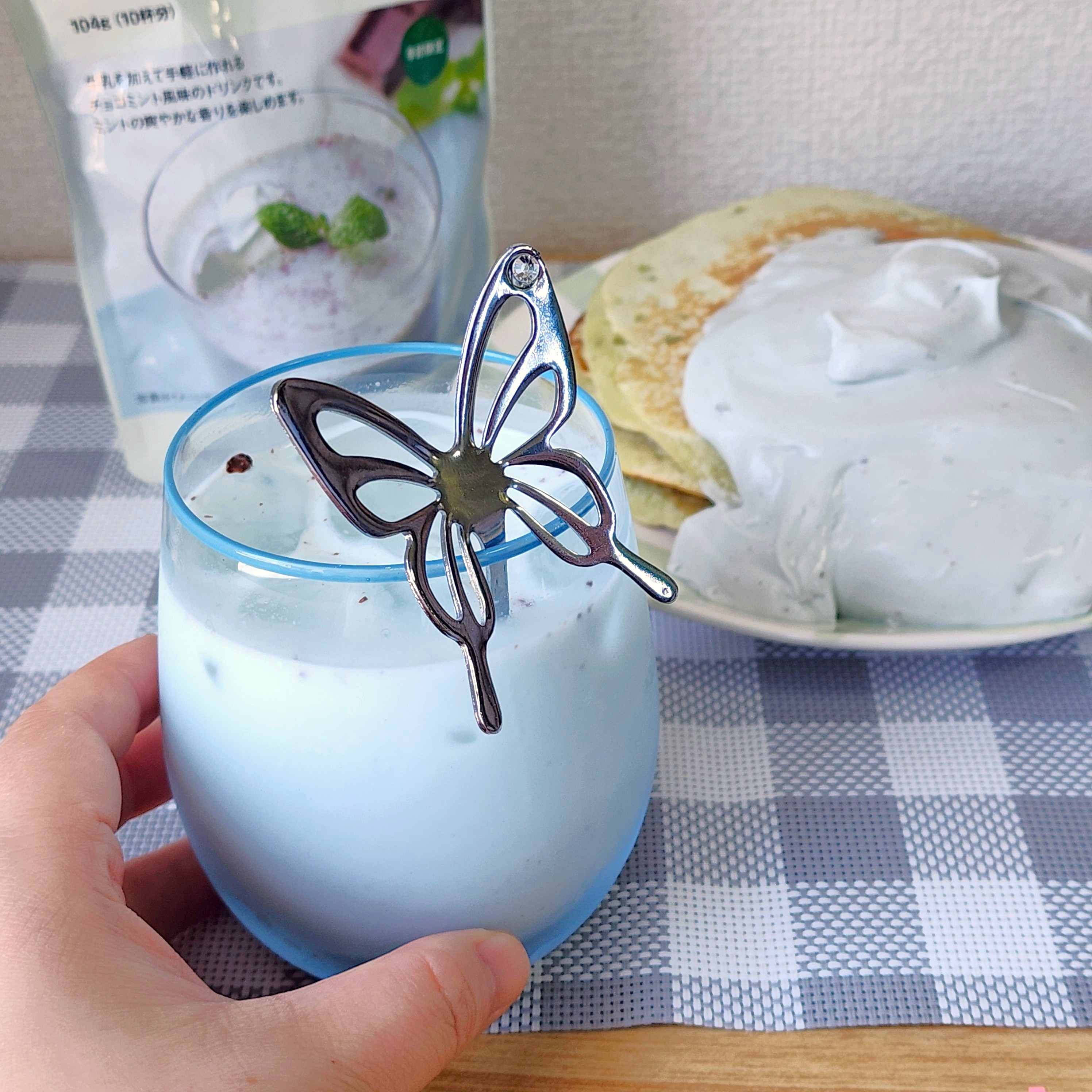 手に持たれたガラスのカップにミントデザートが入っており、バタフライの飾りが添えられている。背景に同じデザートがある。