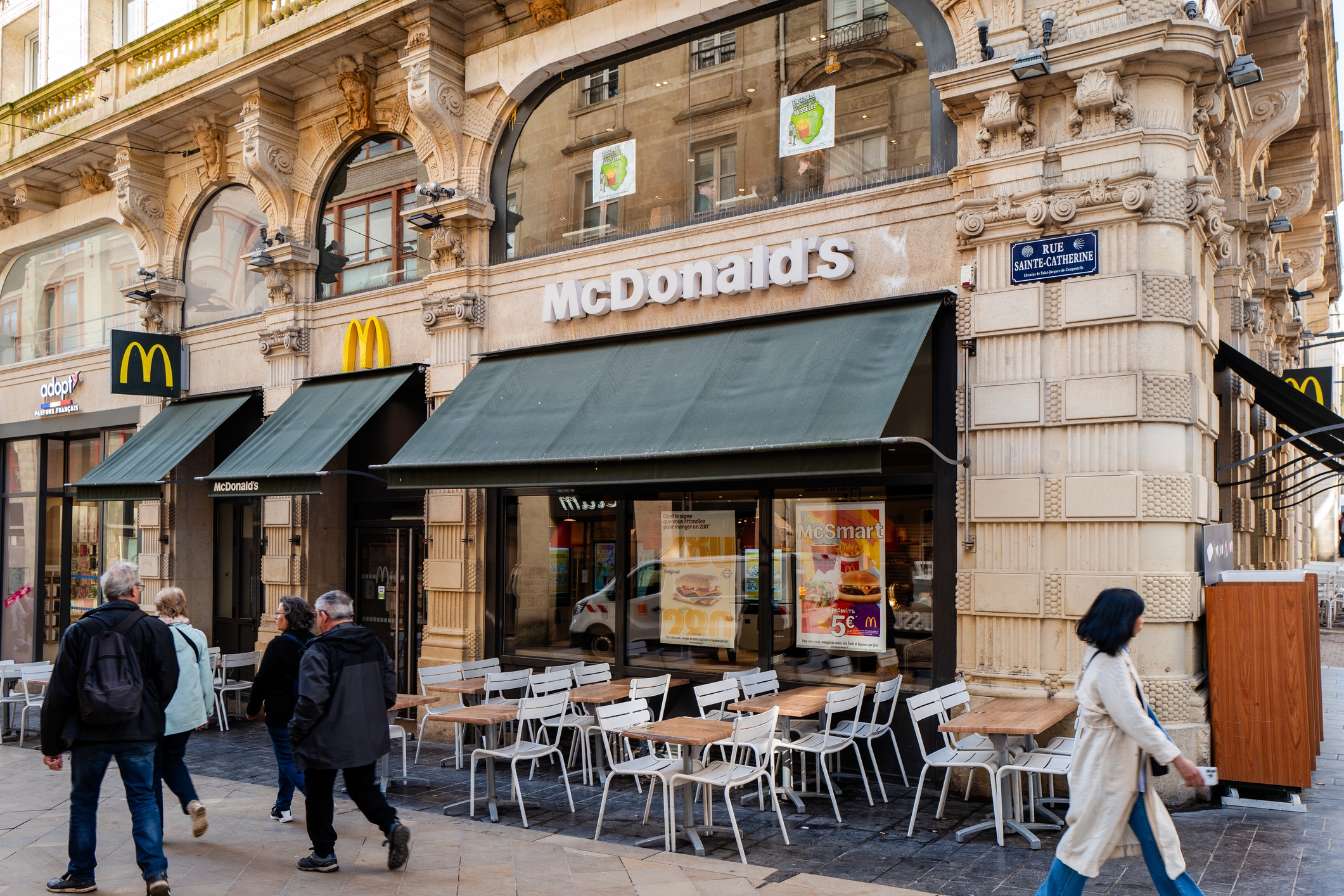 McDonald's restaurant on a busy European street with ornate architecture, outdoor seating, and pedestrians walking by
