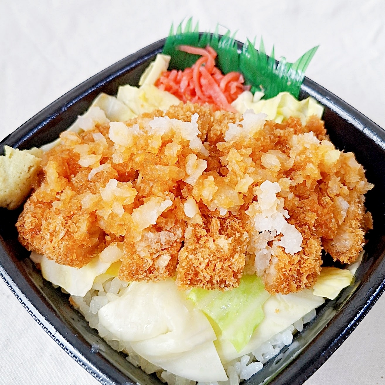 カツ丼が四角い容器に盛られている。ご飯の上にカツ、キャベツ、紅しょうががある。