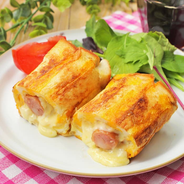 お皿に盛られたチーズが溶け込んだホットドッグ風のパン料理。添えられたサラダも見える。