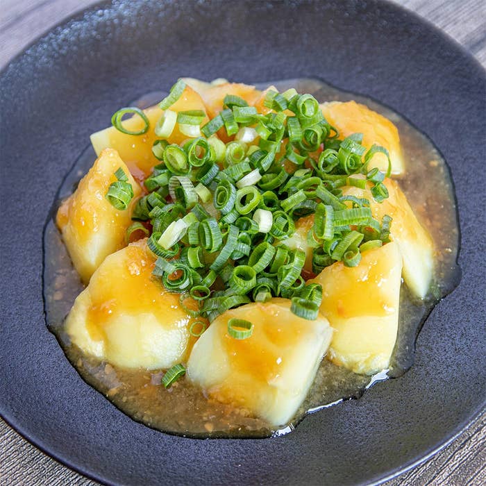 皿に盛られた茹でたジャガイモにタレと刻みネギがかかっている料理。