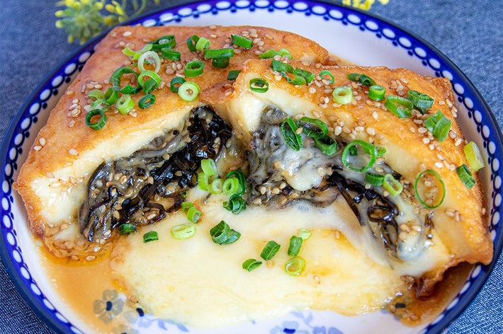 チーズが入った揚げ豆腐にネギと胡麻が散らされている料理が皿に盛られている。