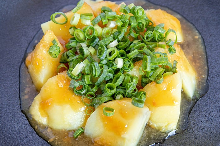 角切りされたじゃがいもの上にきざみネギと透明なソースがかかった料理。黑い皿に盛り付けられている。