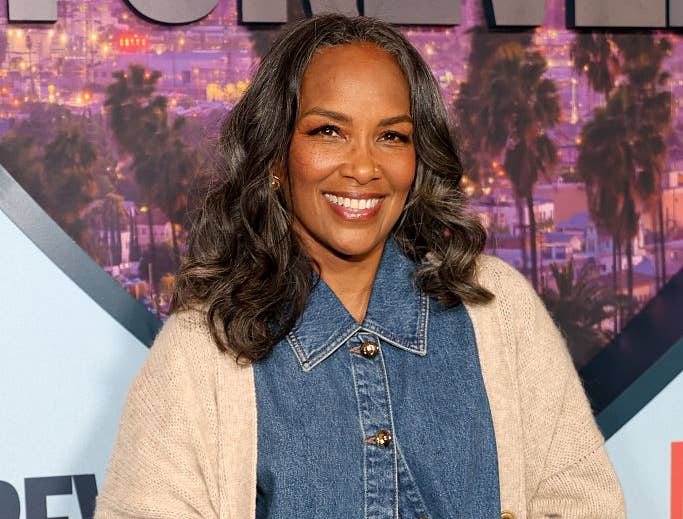 Person in denim outfit with a beige cardigan, smiling at a TVAndMovies event backdrop