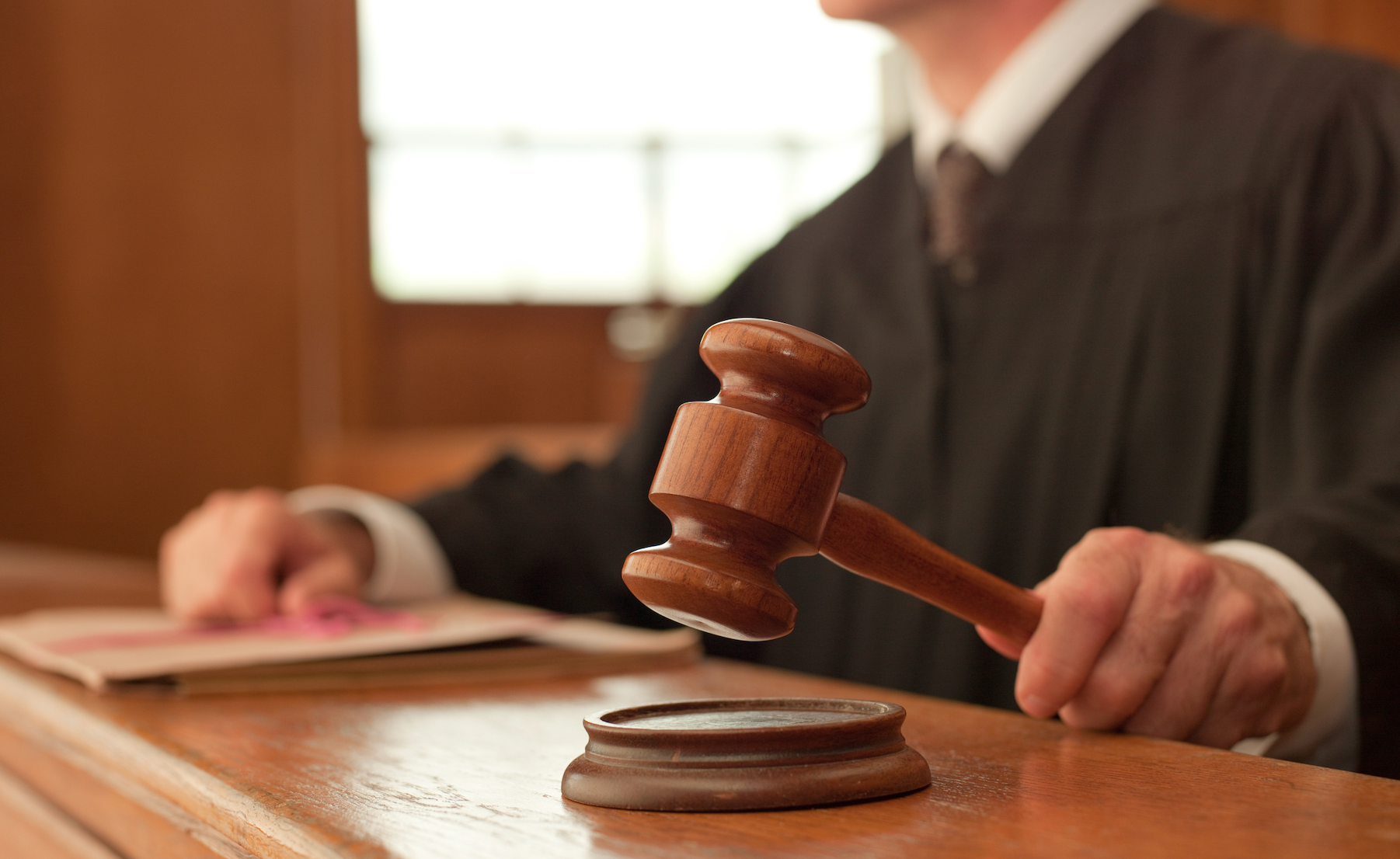 Judge holding a gavel over a wooden block in a courtroom setting, conveying a sense of legal proceedings taking place