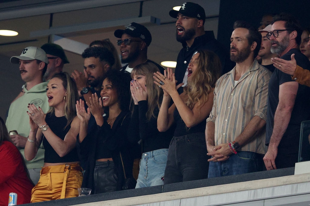 A group of people enthusiastically watches an event from a balcony, clapping and cheering