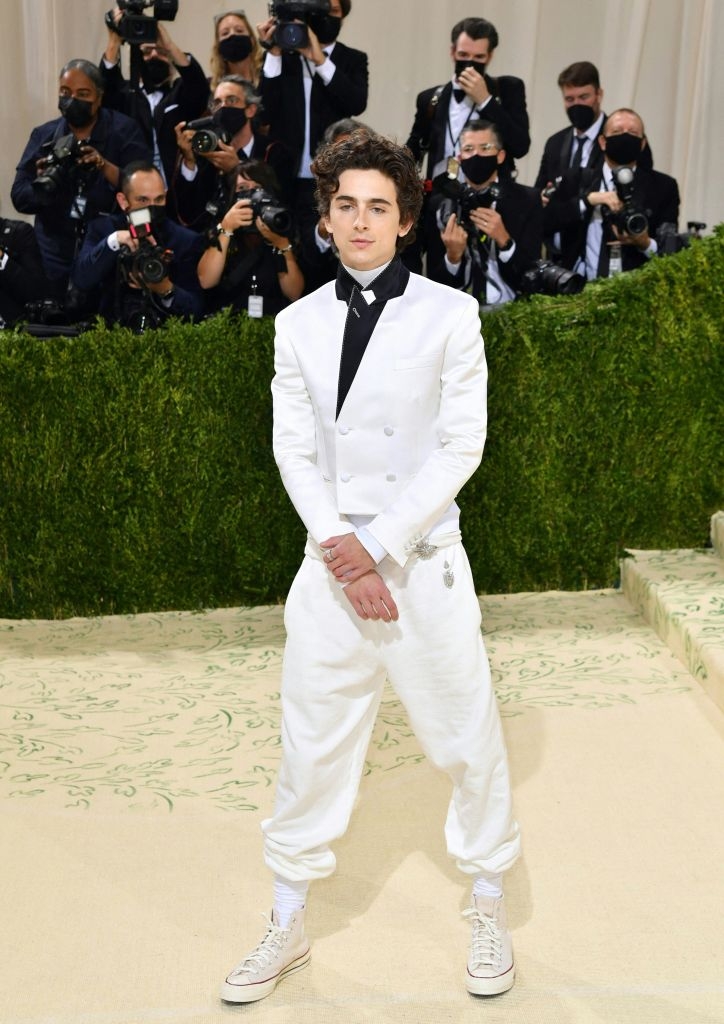 Person in a white double-breasted suit with high-top sneakers at an event with photographers taking pictures in the background