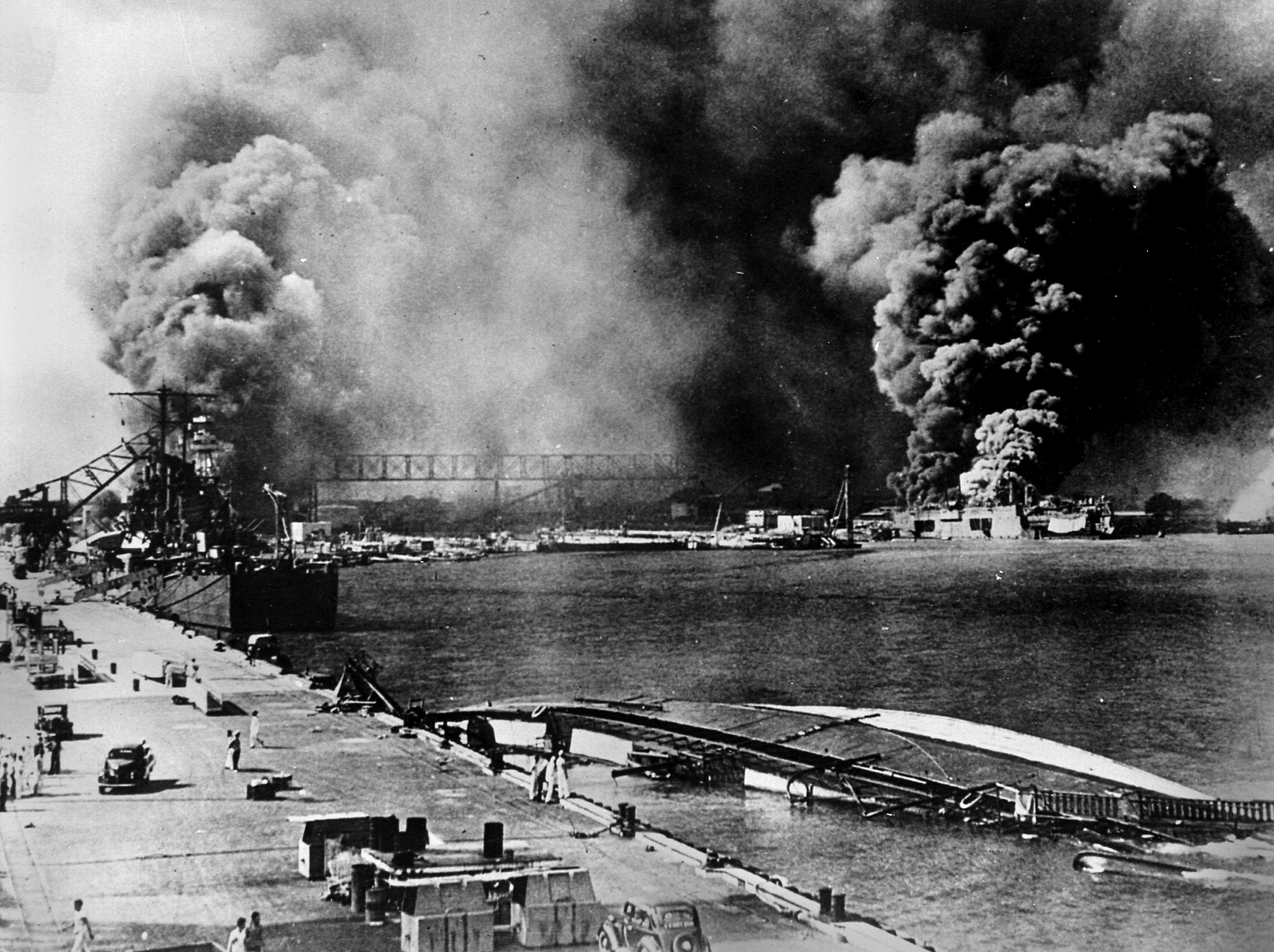 World War II. Pearl Harbor during the Japanese attack of December 7, 1941. On the left, the light cruiser &quot;Helena&quot; hit by a bomb. On the right, workshops and shops on fire.