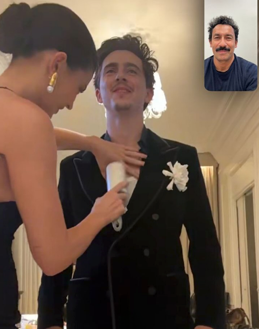 A person in a tailored suit is getting ready with assistance. A video call screen shows someone watching