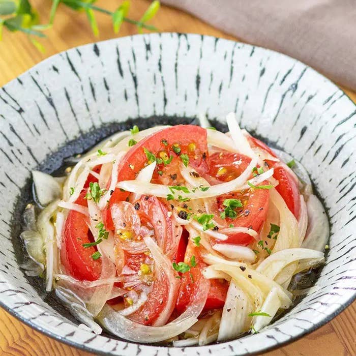 トマトと玉ねぎのスライスが盛られたおしゃれな陶器のボウルに盛り付けられたサラダ。パセリが散らされている。