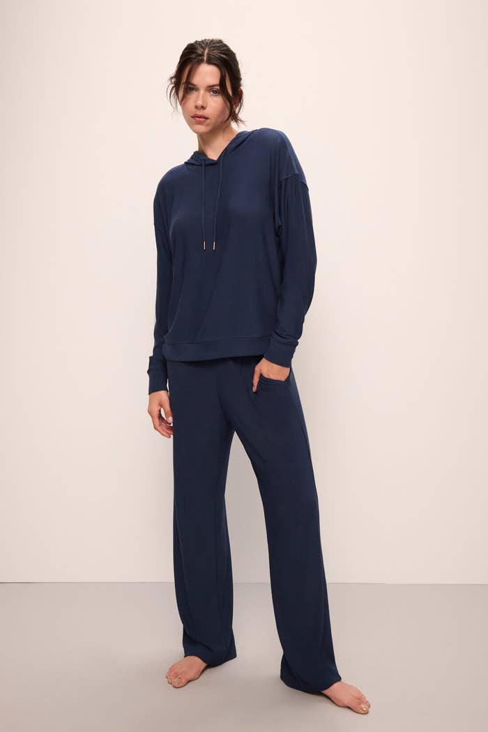 A idiosyncratic successful casual loungewear, including a hooded apical and relaxed pants, posing barefoot against a plain backdrop
