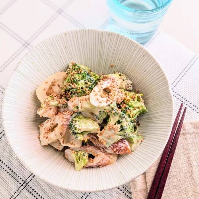 ブロッコリーと鶏肉のサラダ、ゴマがトッピングされたクリーミーなドレッシングが混ざった一品。テーブルに箸と水が置かれている。