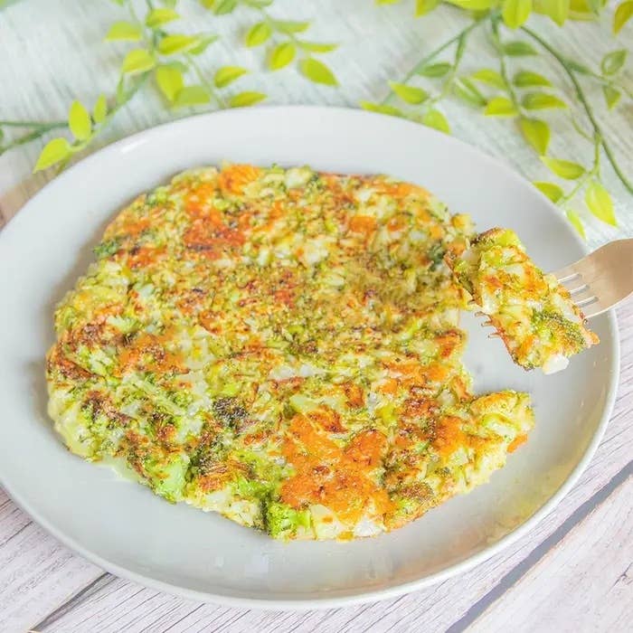 フォークに取られた一口分の野菜たっぷりのお好み焼きが白い皿に乗っている。背景に植物の装飾が見える。