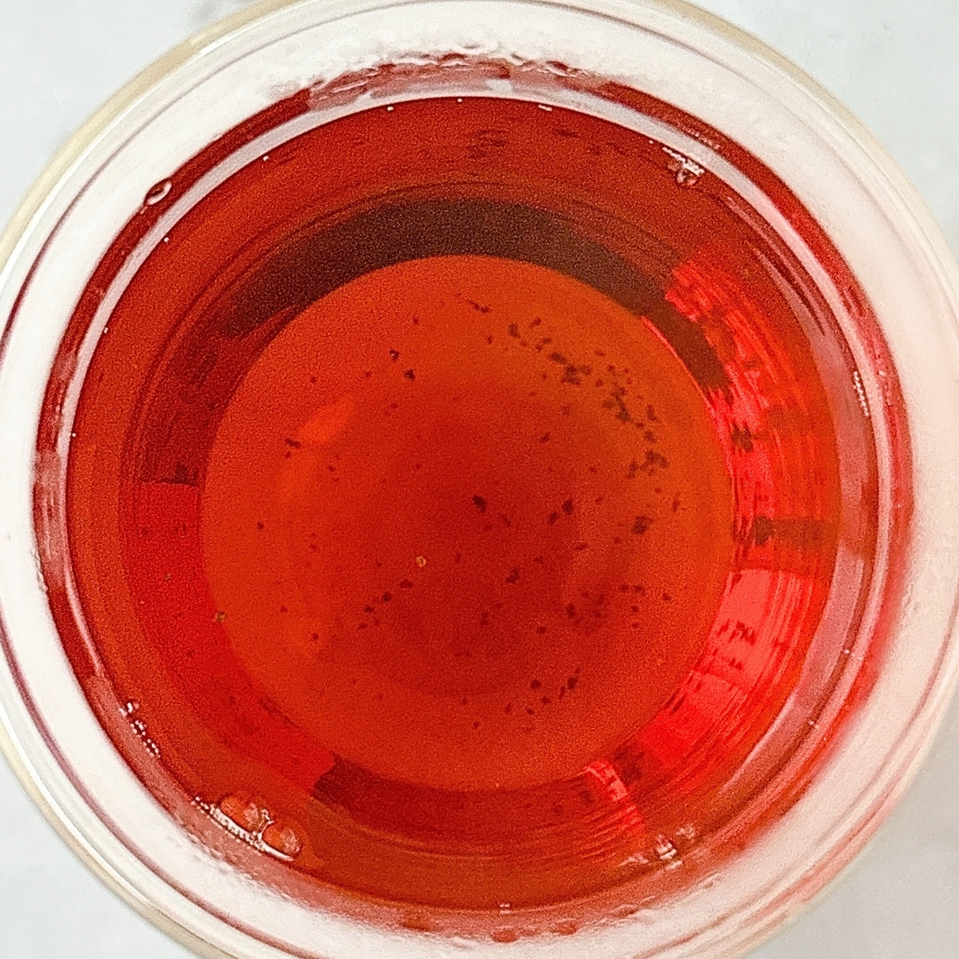 透明のグラスに入った赤い液体の飲み物を上から見た図。液体の表面には小さな黒い粒が浮かんでいる。