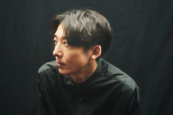 Person with short hair looks to the side, wearing a button-up shirt against a dark background