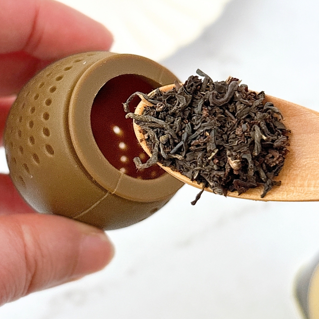 木のスプーンに載った紅茶の葉と茶こしを手に持っている様子。茶葉の香りを示唆する。