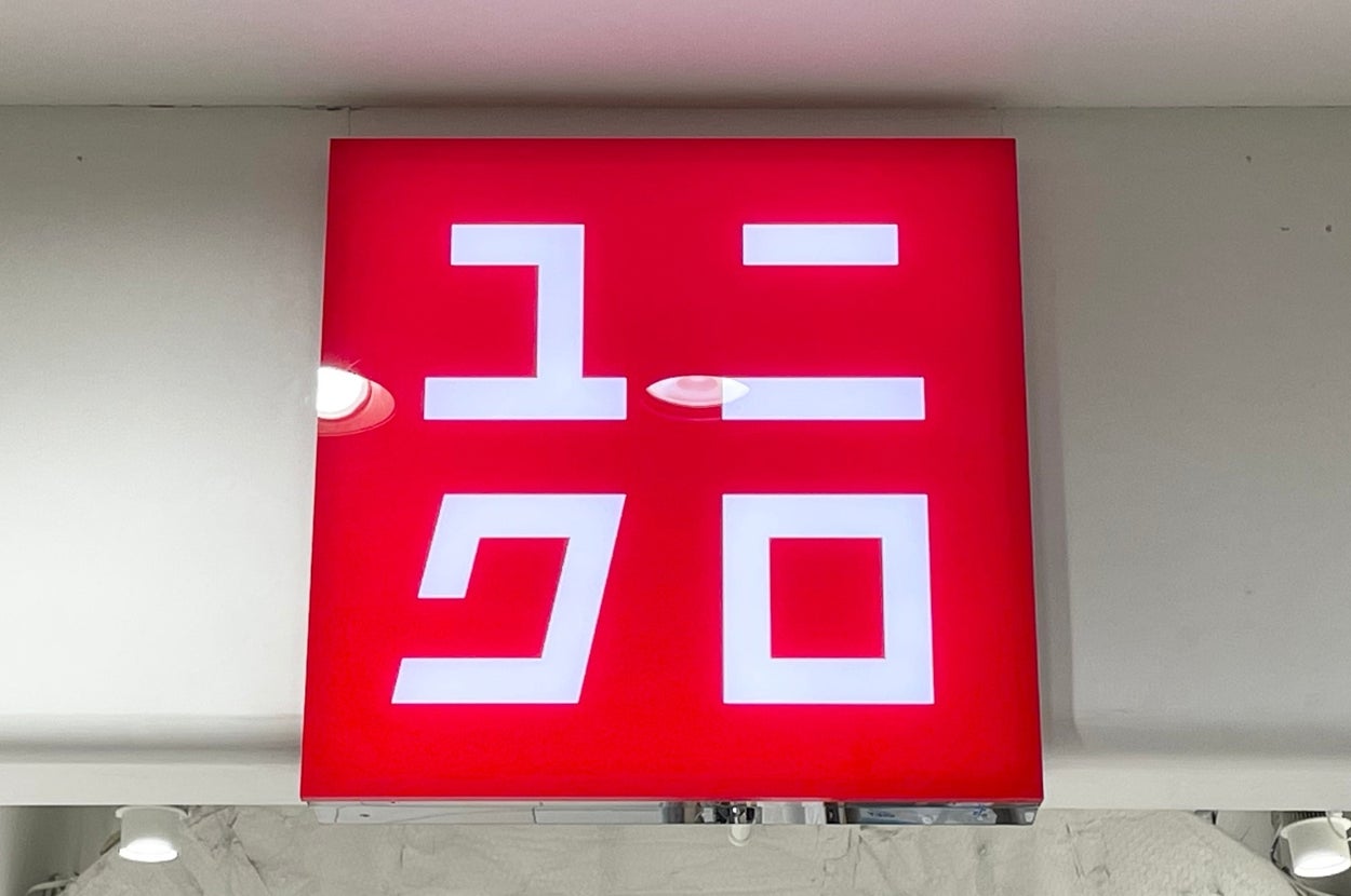 Red Uniqlo sign with Japanese katakana characters, mounted on a store ceiling with visible air vents and lights