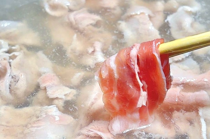 しゃぶしゃぶ鍋で箸に取られた薄切り肉。温かい料理の一部を示す。