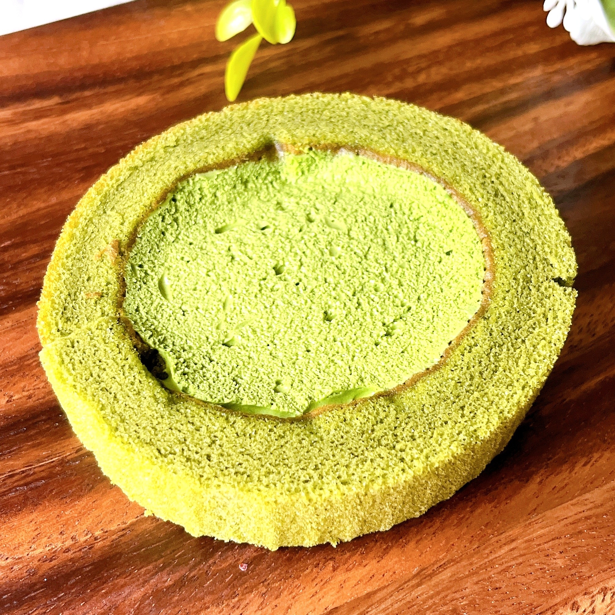 抹茶味のロールケーキが木製のテーブル上に置かれている。シンプルで美しいスイーツ。