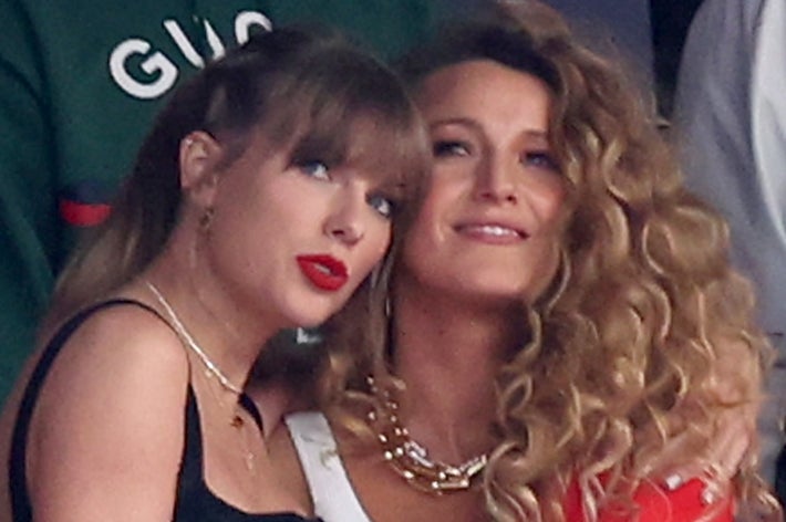 Four women stand together at an event. The third wears a black dress, and the fourth wears a sporty red outfit with a white-striped jacket