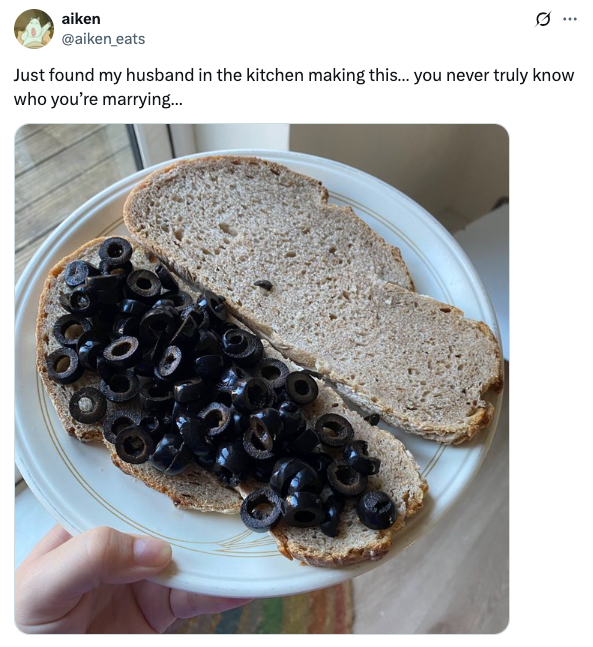 Two slices of bread on a plate, one topped with a pile of black olives