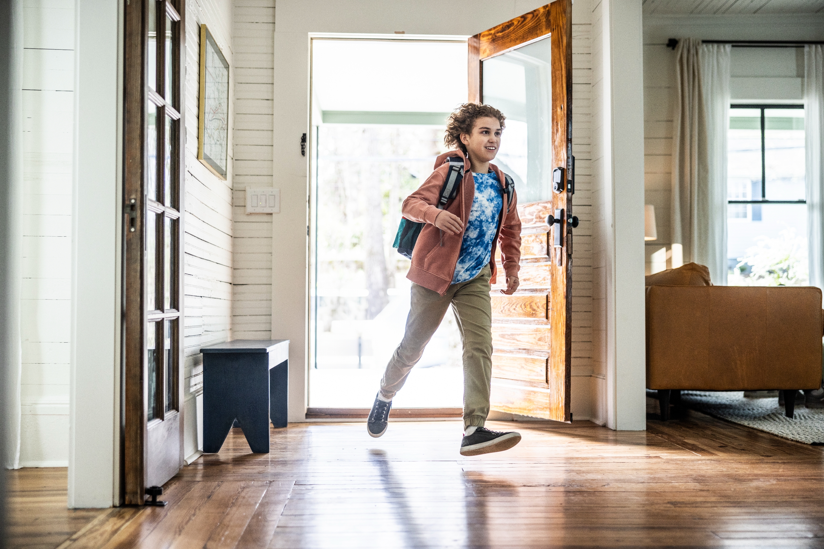 Person enthusiastically enters a living room, wearing casual attire with a backpack, suggesting arrival or return home