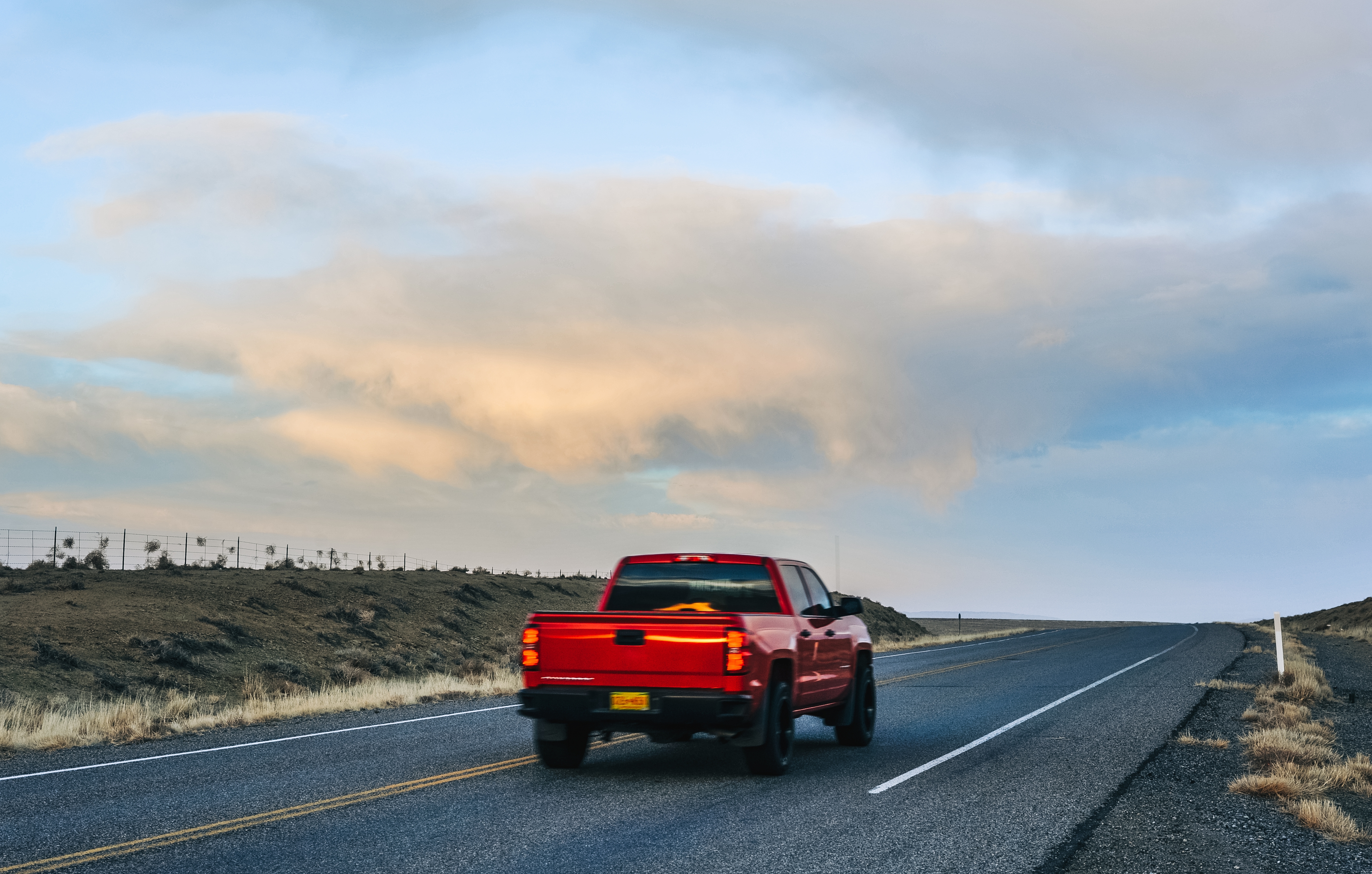 Red truck driving on an empty road through a rural landscape under a cloudy sky