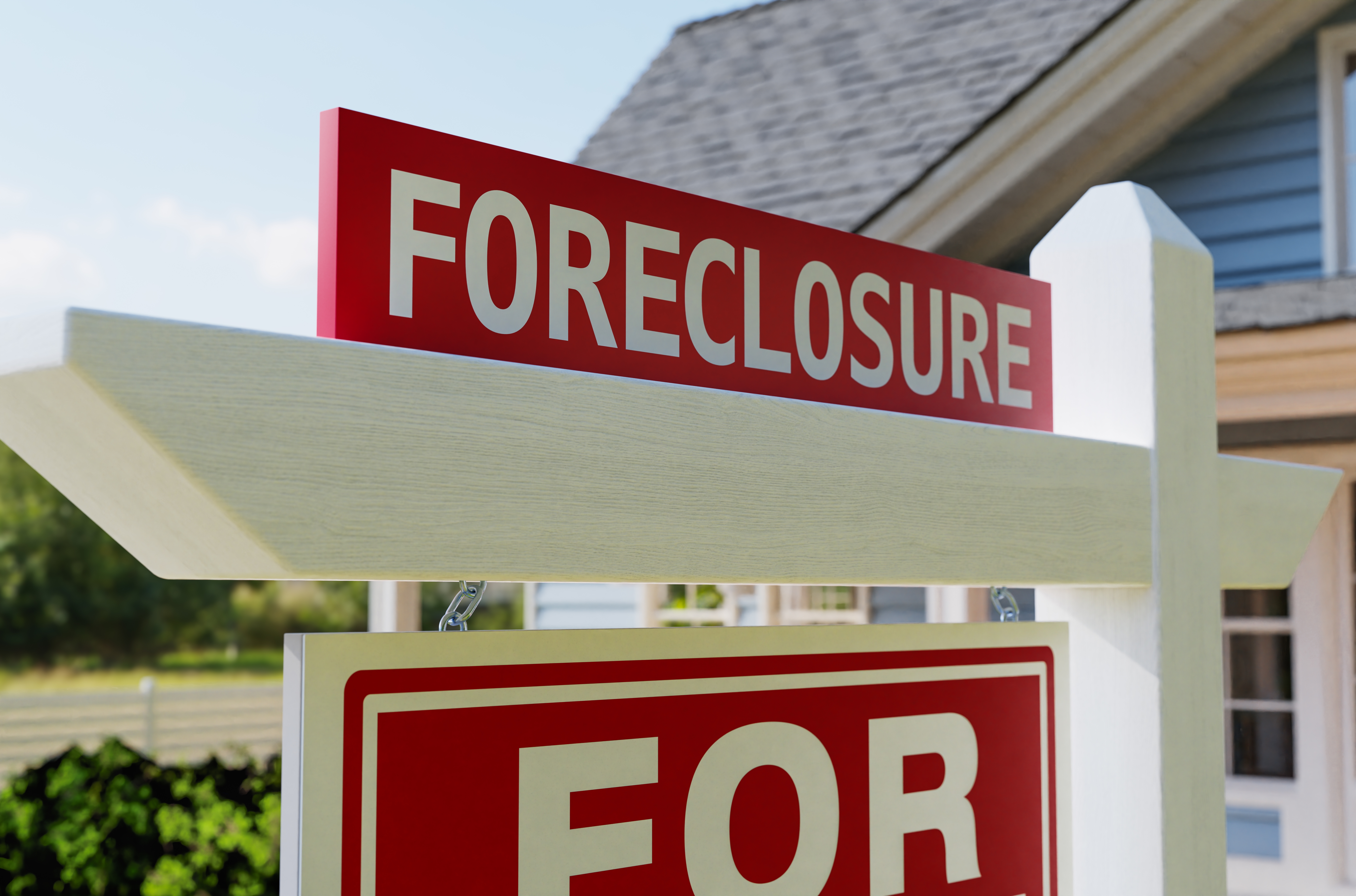 Foreclosure sign in front of a house, indicating the property is for sale due to foreclosure