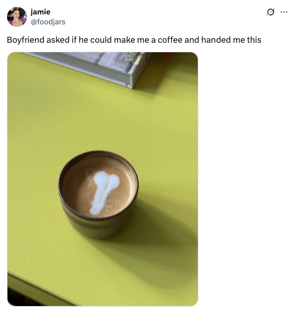 A cup of coffee with latte art resembling a humorous, abstract shape on a table