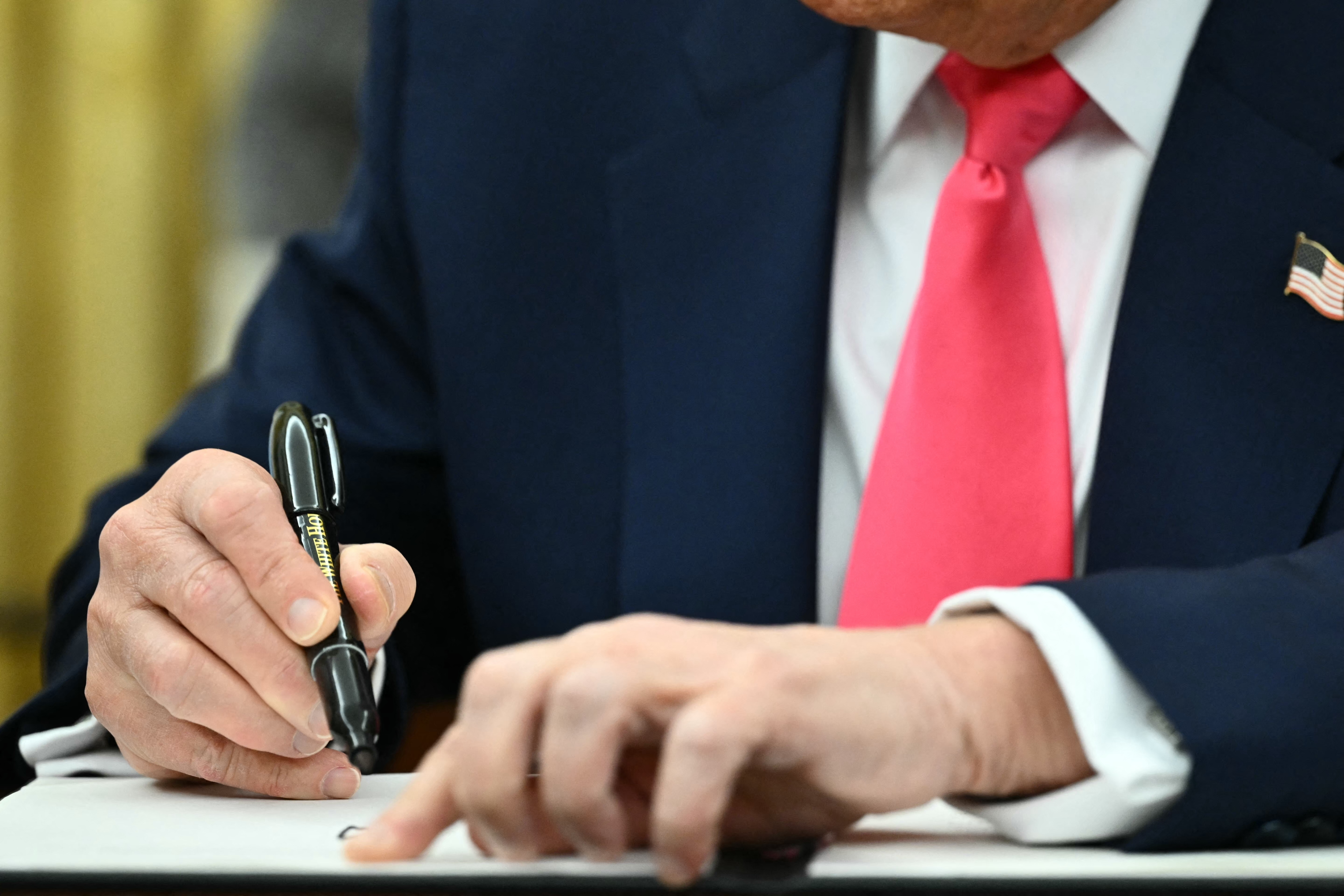 Person in business attire, with a flag pin, signing a document with a black pen