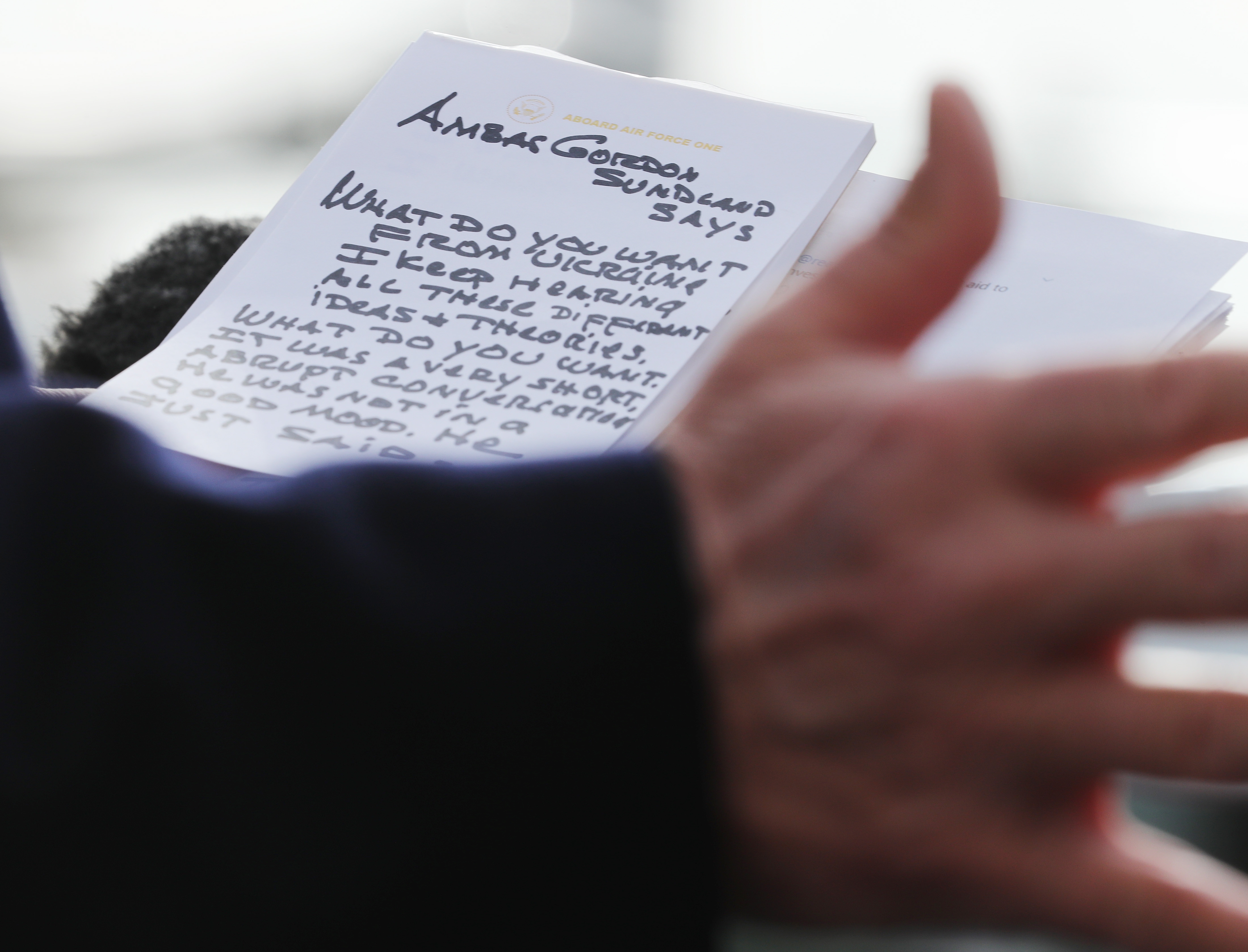 A person holds a notepad with handwritten notes about inquiry questions related to Amb. Gordon Sondland