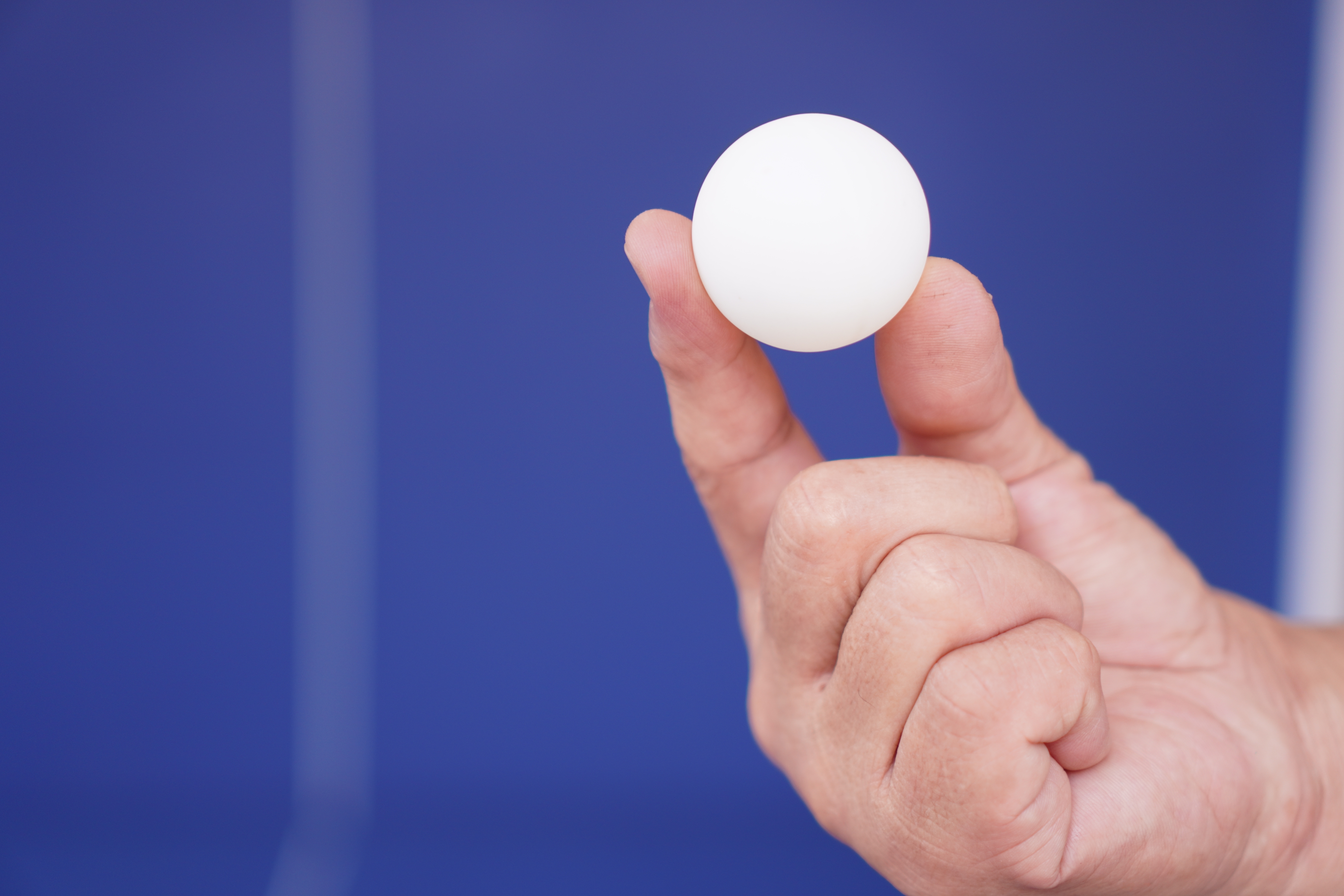 A hand holds a small, round object, possibly a ping pong ball, against a plain background