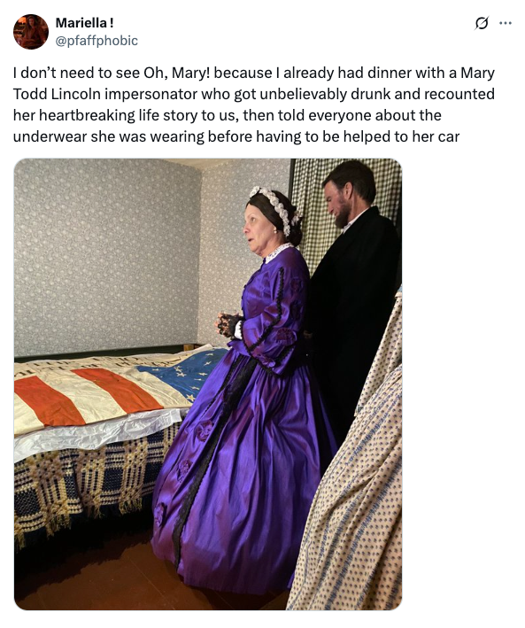 Person dressed as Mary Todd Lincoln stands in a room with a quilted bed, accompanied by another person