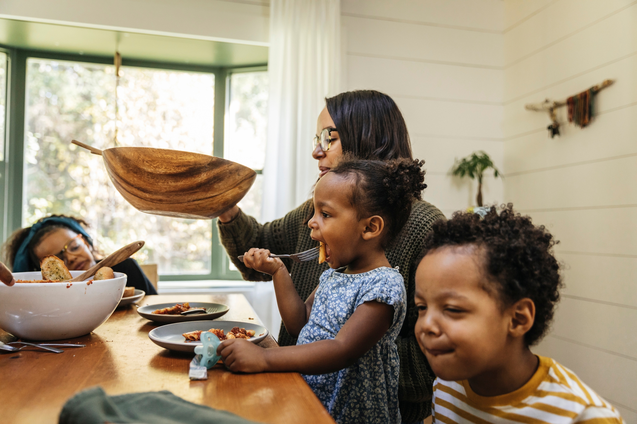 A family eating together at a table, with a woman serving food and two children eating and smiling