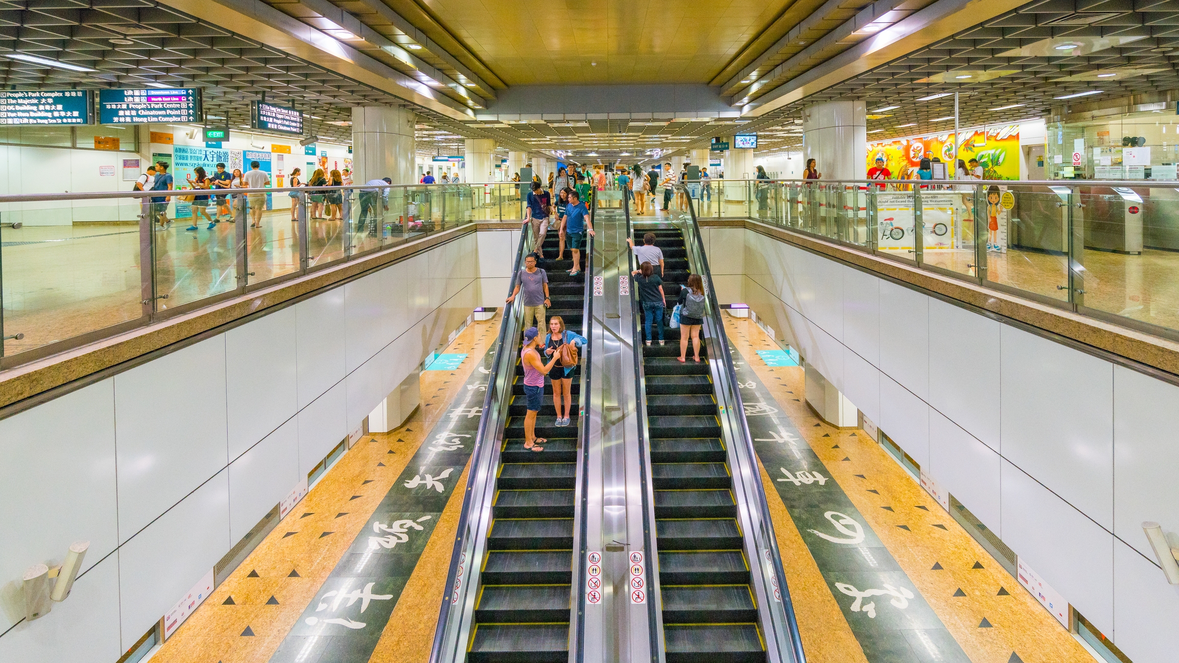People use escalators in a busy subway station with signs and s on the walls