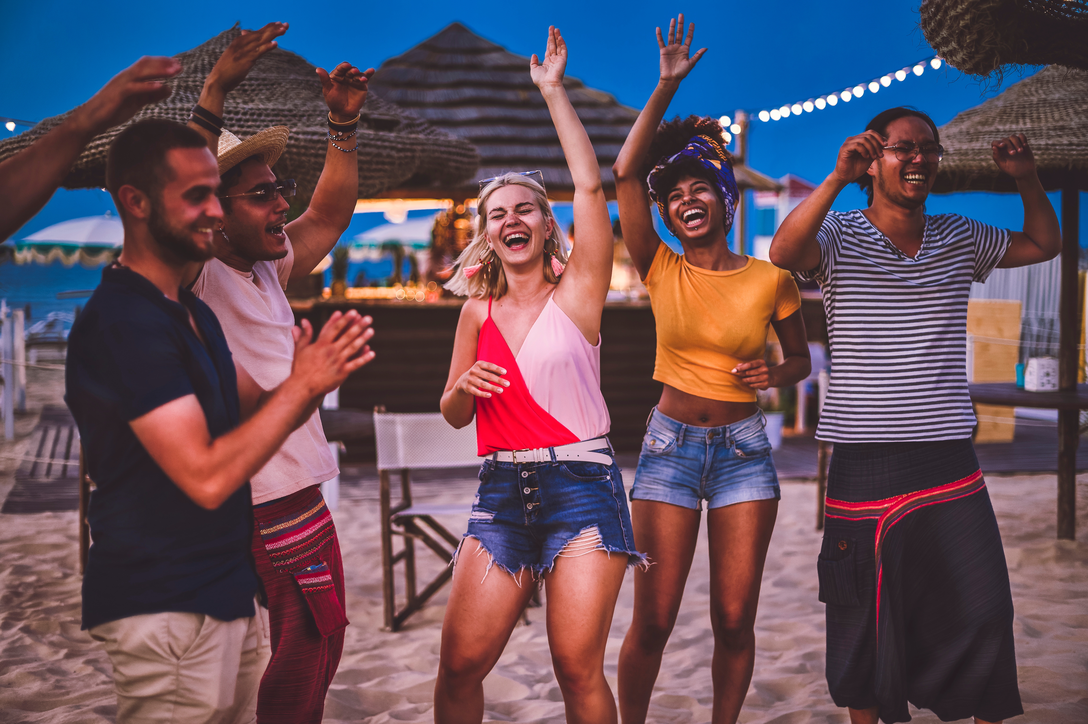 People joyfully dancing at a beach party with string lights in the background