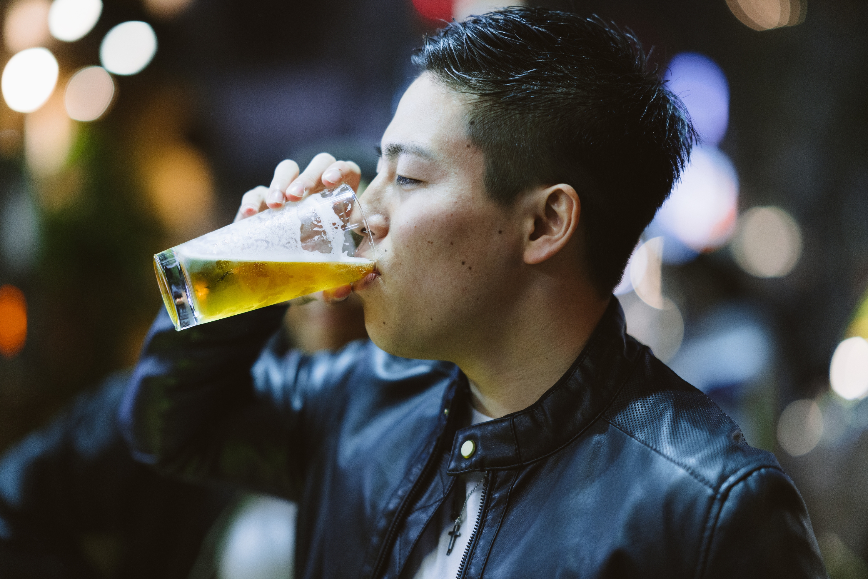 Person drinking a glass of beer in a casual setting, wearing a leather jacket