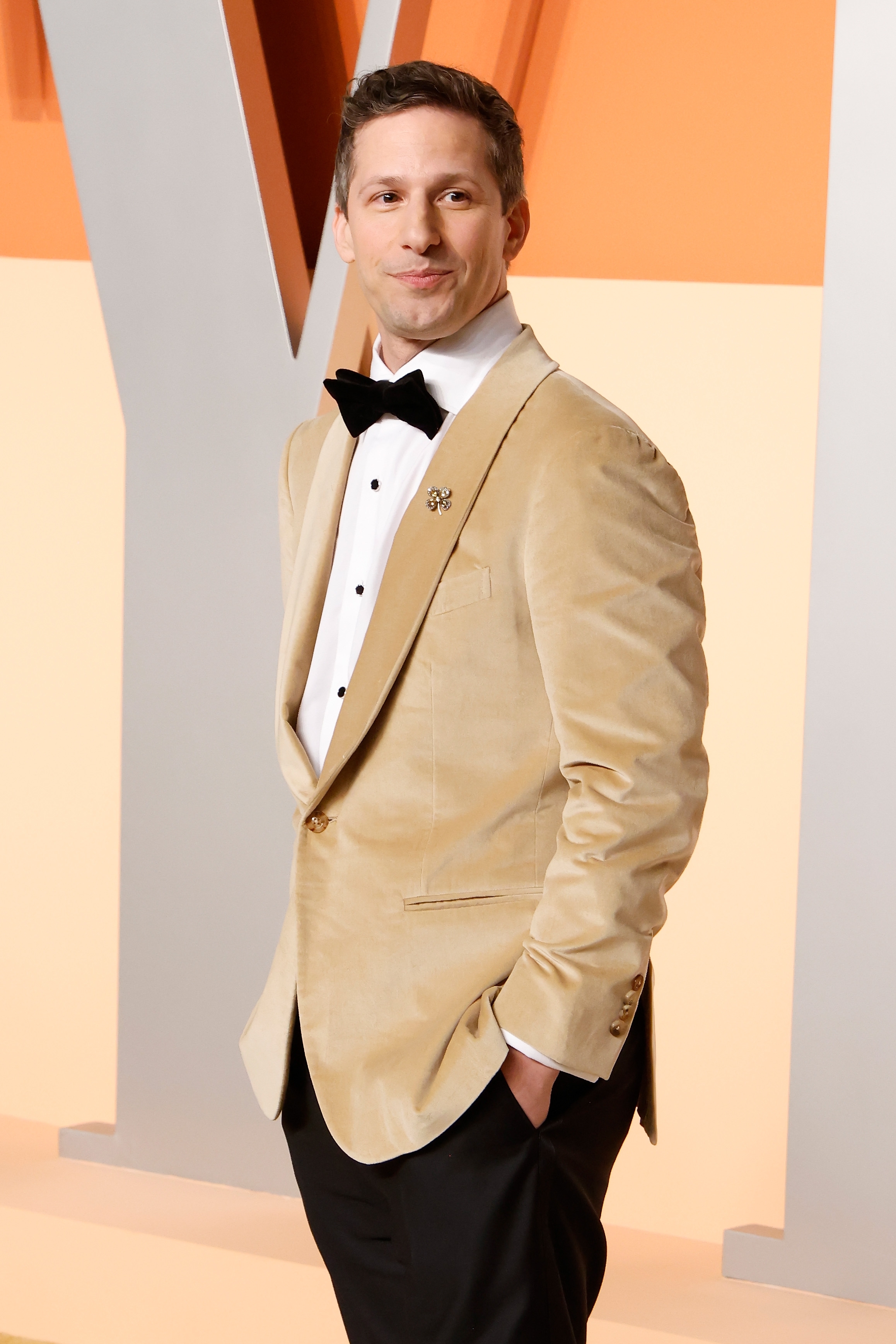A person in a light suit with a black bow tie and white shirt poses at a formal event, standing casually with one hand in a pocket