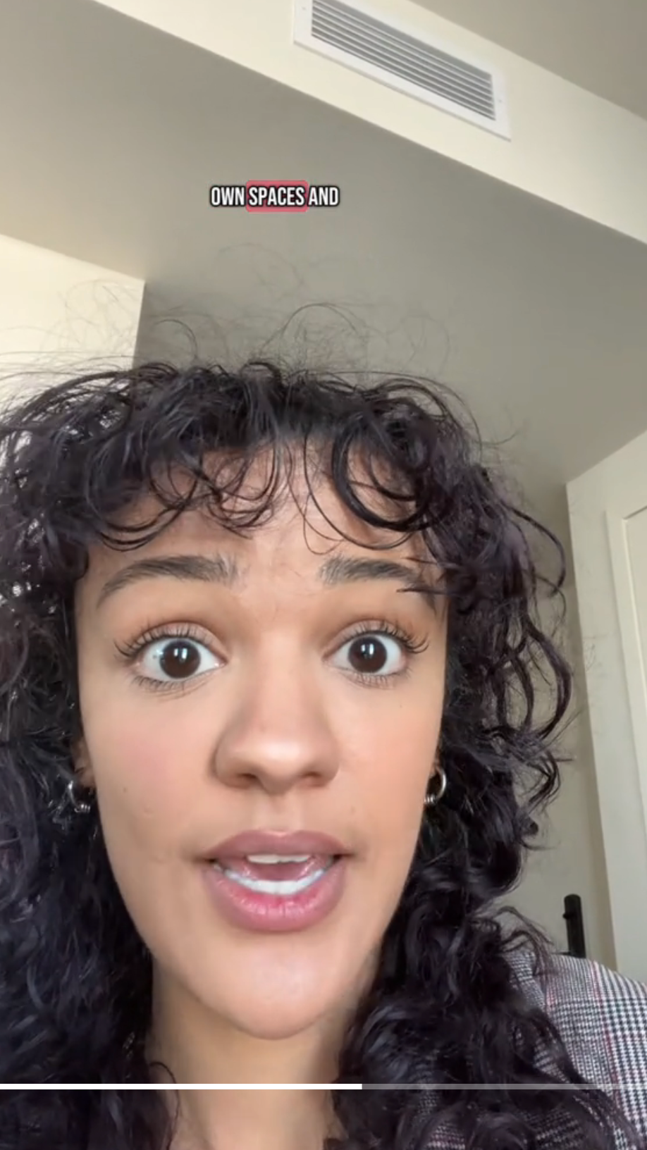 Person with curly hair speaks in a video. Visible text reads, "OWN SPACES AND."