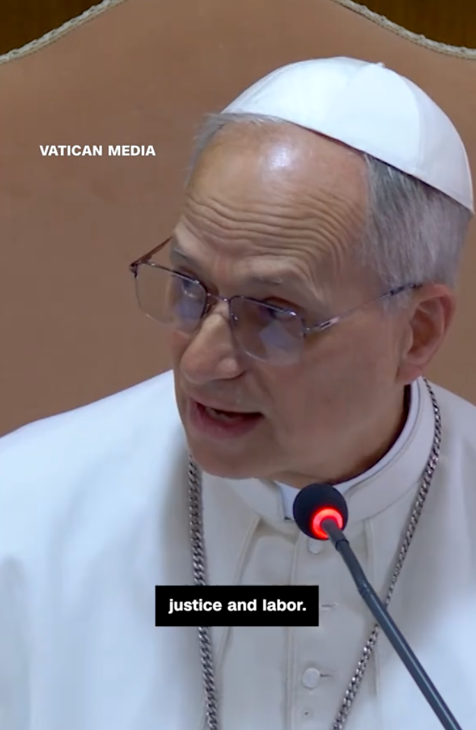 A religious leader, dressed in traditional attire, speaks into a microphone. The text overlay mentions "justice and labor."