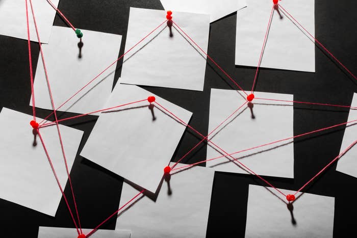 Pinned papers connected by red strings, forming a grid pattern on a dark surface. 