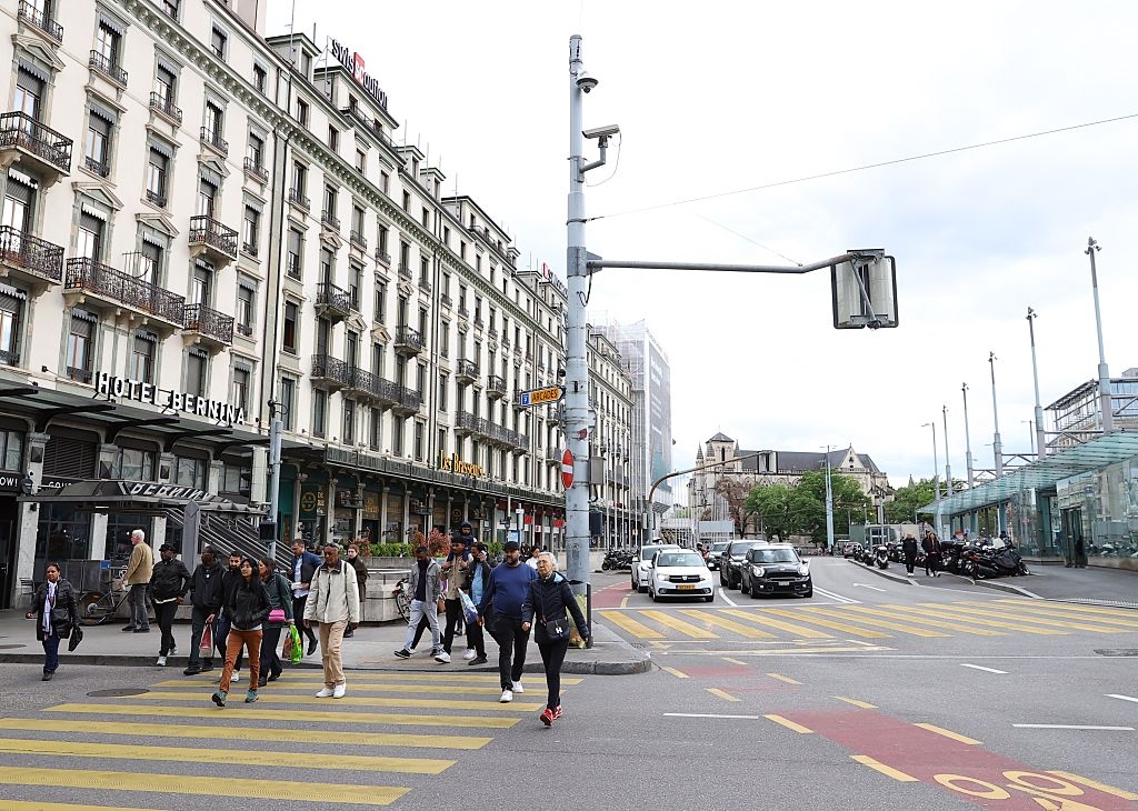 People crossing a city street at a busy intersection with buildings and cars in the background