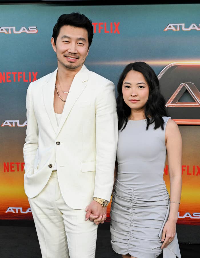 A man in a white suit and a woman in a sleeveless dress pose together at a Netflix red carpet event