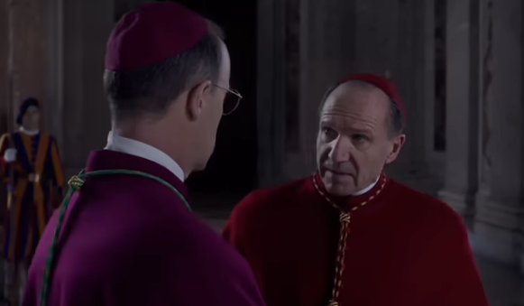 Two men in religious attire converse inside a grand building, with Swiss Guards standing in the background