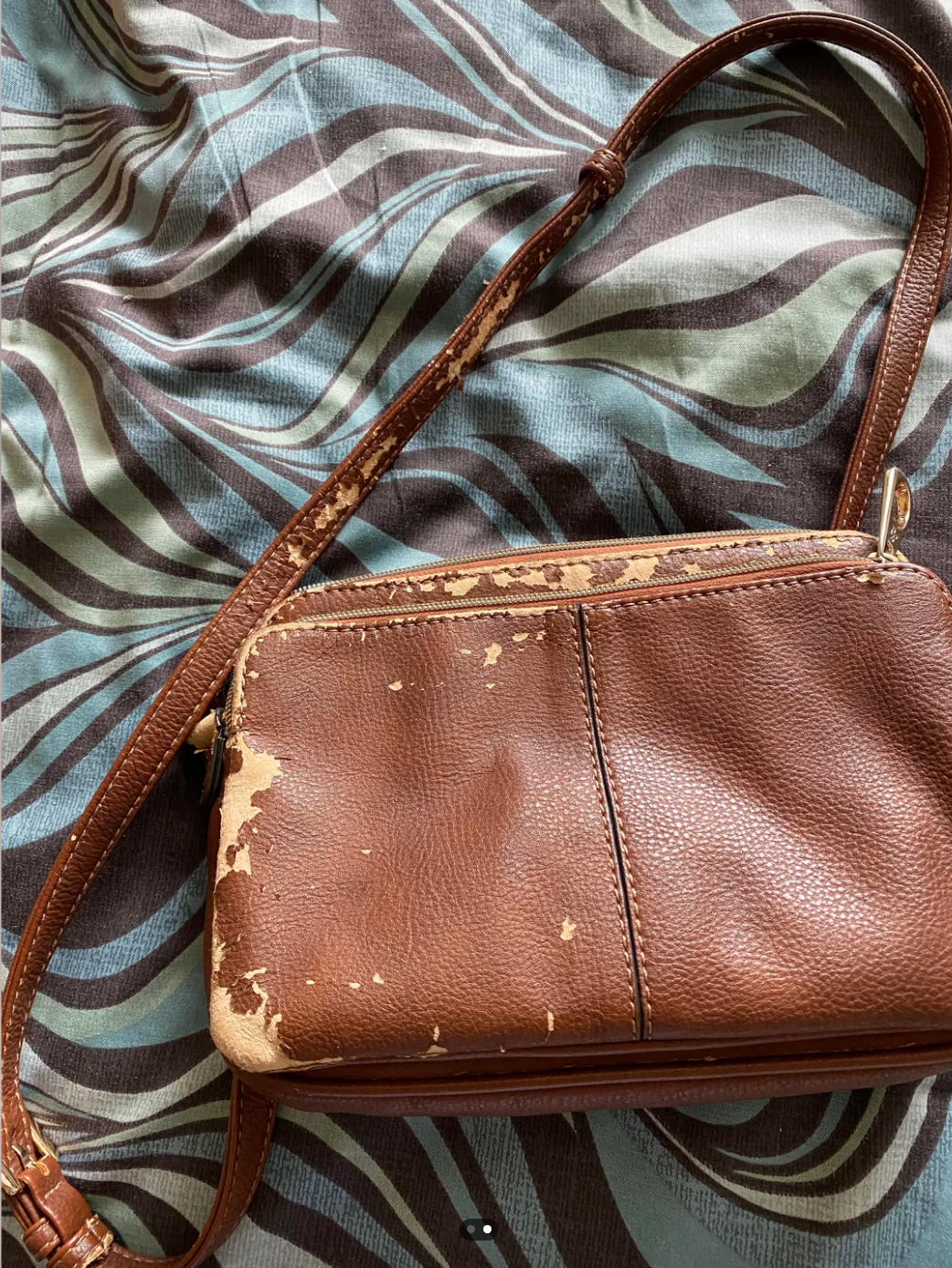 Worn leather handbag with peeling surface, resting on a striped fabric background