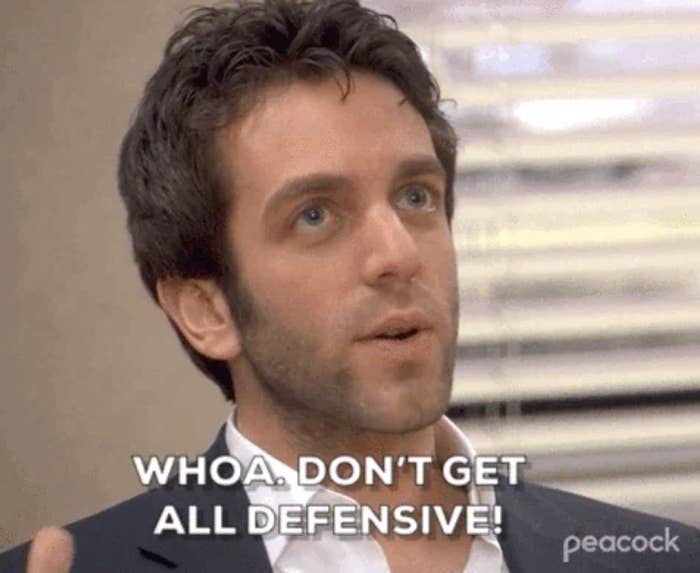 A person with dark hair and suit says, "Whoa. Don't get all defensive!" in an office setting, conveying surprise or disbelief